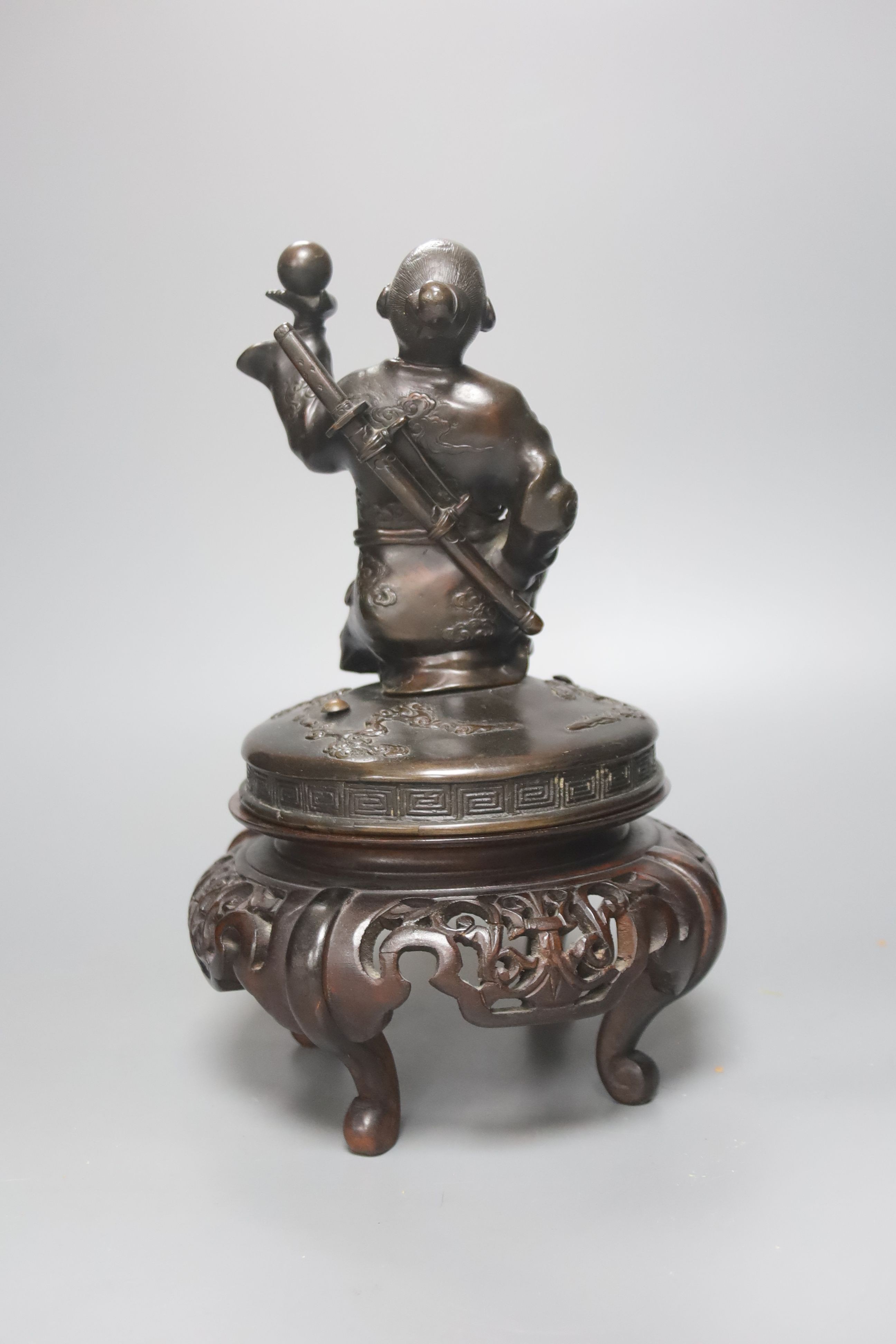A Japanese bronze cover modelled as a samurai general, Meiji period, holding a fan and a ball, wood stand 28cm total height